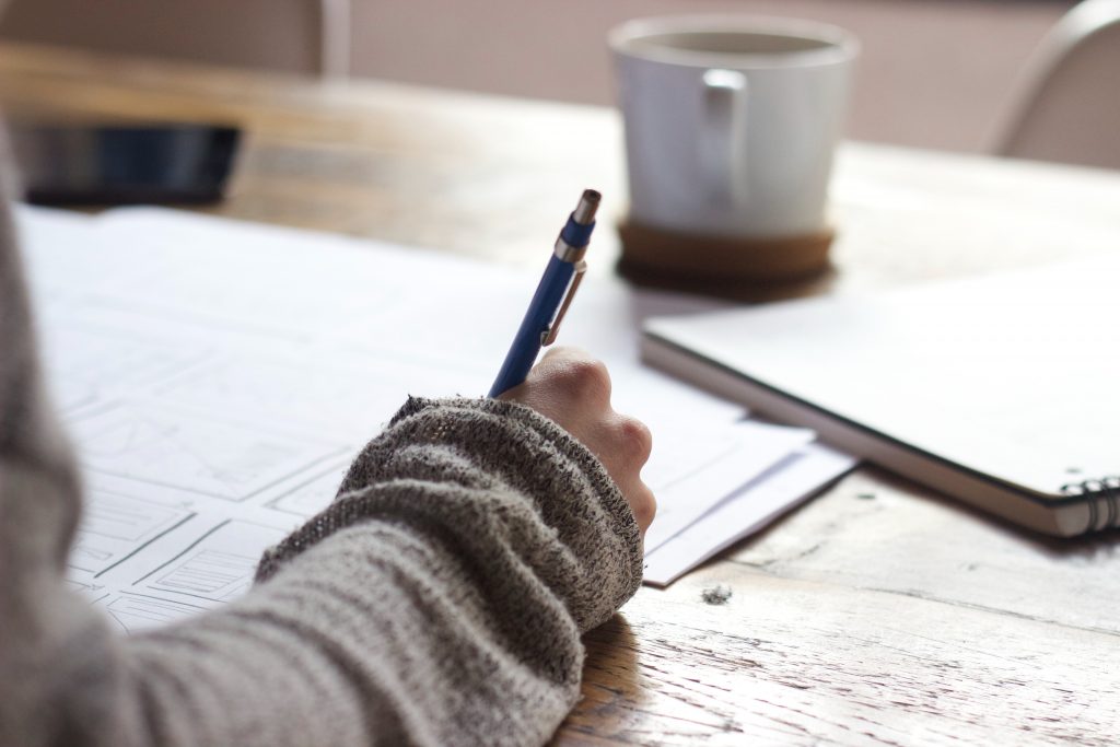 Somenoe writing with a pen on paper, with a cup of coffee nearby