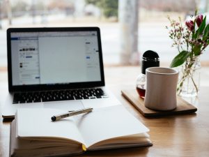 An open laptop with a pen and paper and a cup of coffee